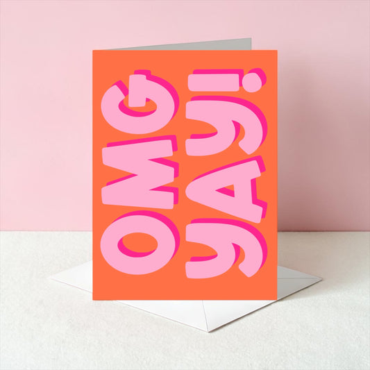 Orange card with pink text 'OMG YAY!' on a white surface with a pink background